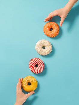 Two hands reach for donuts on blue background, top view. Creative layout with delicious glazed donuts. Vertical flat lay with diagonal made from donuts or doughnuts