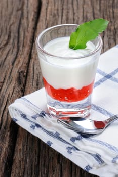 fresh natural yogurt with strawberry jam in glass on wooden plank