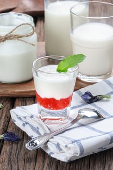 fresh natural yogurt with strawberry jam in glass on wooden plank
