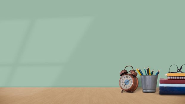 Mock up of student's desk with book, pencil and clock on green wall background . High quality photo