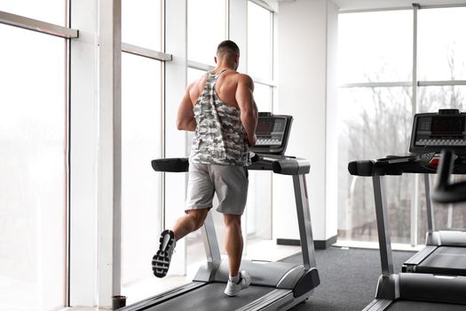 Muscular athletic bodybuilder fitness model running treadmill gym near big window jogging stationary machine do cardio training Weight loss Healthy lifestyle concept. Back view rear full length