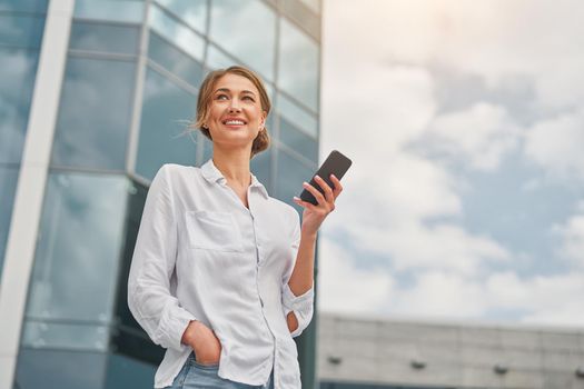 Businesswoman successful woman business person standing outdoor corporate building exterior cell phone Pensive elegance cute caucasian professional business woman middle age dreaming with mobile phone