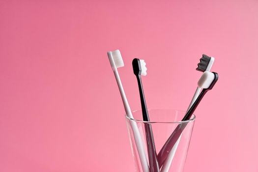 Fashionable toothbrush with soft bristles. Popular toothbrushes. Hygiene trends. Kit of toothbrushes in glass on pink background.