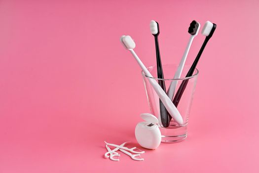 Fashionable toothbrush with soft bristles. Popular toothbrushes. Hygiene trends. Oral hygiene kit. Toothbrushes in glass, floss thread and toothpicks on a pink background.