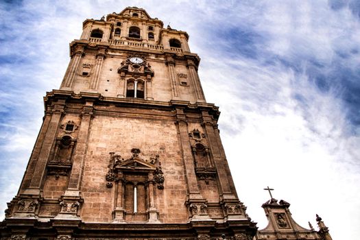 Tower bell, clock and carved stone details on the facade of the Cathedral of Murcia.