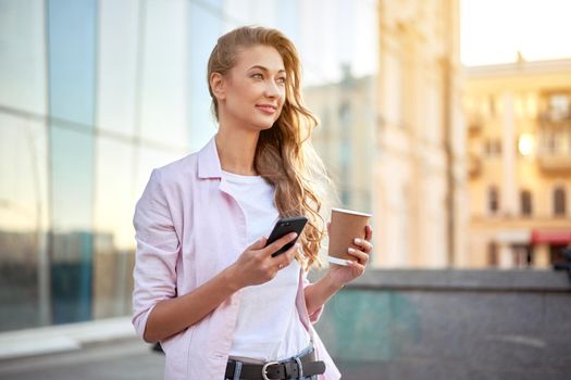Businesswoman standing summer day near corporate building using smartphone teeth smiling Business person Outdoors Successful european caucasian woman freelancer dressed white shirt pink jacket