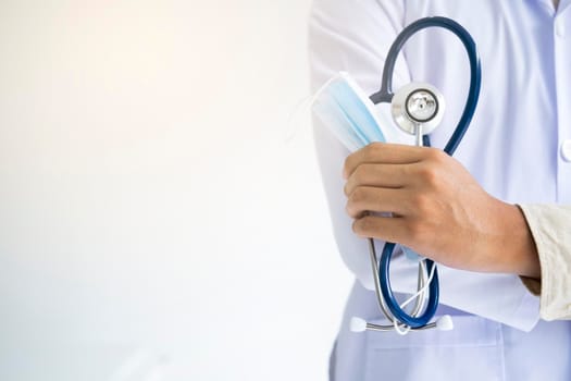 Young man doctor holding stethoscope and medical mask to protect against coronavirus 2019 disease or COVID-19 global outbreak.