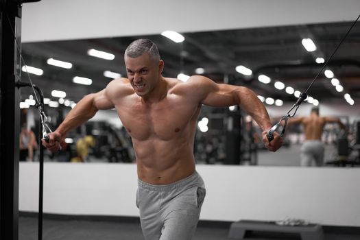 Muscular athletic bodybuilder standing training chest and shoulders muscles on fitness equipment wire cable machine Sport fitness healthy lifestyle Man do flyes exercises on gym machine
