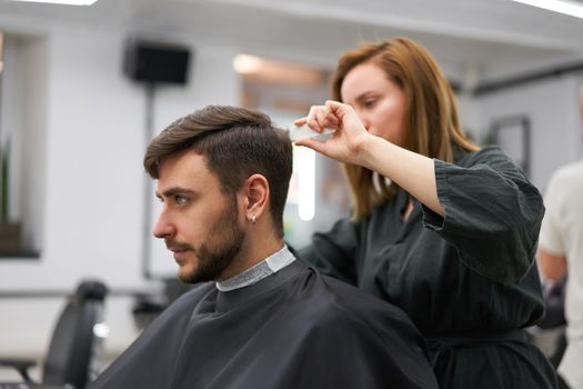 Stylish man sitting barber shop Hairstylist Hairdresser Woman cutting his hair Portrait handsome happy young bearded caucasian guy getting trendy haircut Attractive barber girl working serving client
