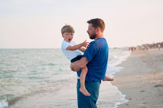 Father son spending time together sea vacation Young dad child little boy walking beach Fathers day. Family with one child. Happy childhood with daddy. sitting on hands laughs