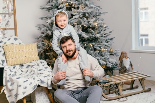 Holiday Christmas Handsome father playing with small cute son near decorated New year tree at home. High quality photo