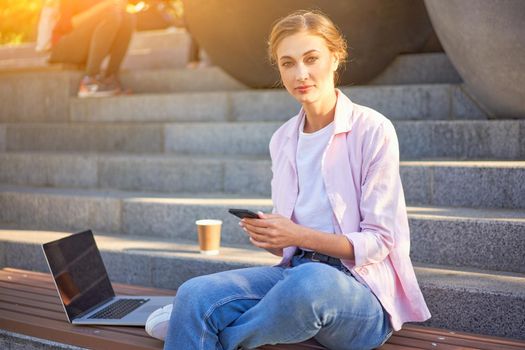 Businesswoman sitting stairs summer park using laptop and smartphone Business persone working remote. Outdoor. Successful Young european caucasian woman freelancer meeting online