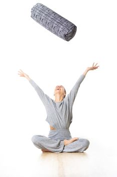 Restorative yoga with a bolster. Young sporty female yoga instructor in bright white yoga studio, throwing bolster cushion in air , smilling, showing love and passion for restorative yoga.