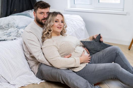 Happy family concept. Husband hug belly pregnant wife sitting floor indoor living room near sofa Caucasian man and woman pregnancy and new life concept. Love and care