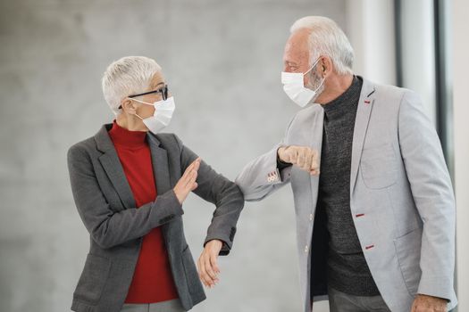 A two senior business people greeting with bumping elbows in a modern office during corona virus pandemic to avoid handshakes.