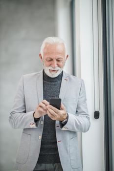 Portrait of a smiling senior businessman using app on smart phone while standing in a modern office.