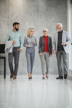 A group of confident business people walking along modern office corridor and discussing project on move.