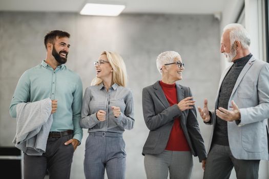 A group of confident business people walking and talking in a modern office hall during the day and looking with smile.