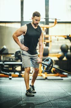 Shot of a muscular guy in sportswear working out with barbell at the cross training gym. 