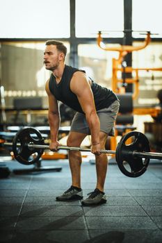 A muscular guy in sportswear working out with barbell at the cross training gym. 