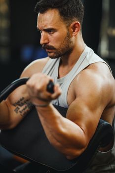 A muscular guy in sportswear working out at the cross training gym. He is pumping up biceps muscule with heavy weight.
