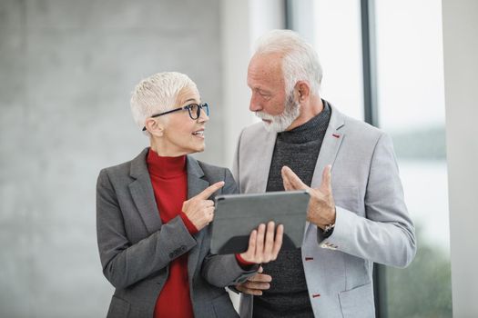 A successful senior businessman and his mature female colleague using a digital tablet in a modern office.