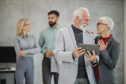 A two successful senior businesspeople using a digital tablet during meeting in a modern office.