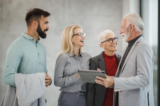 A group of smiling business people using digital tablet  and having a discussion with each other during the meeting in a modern office.