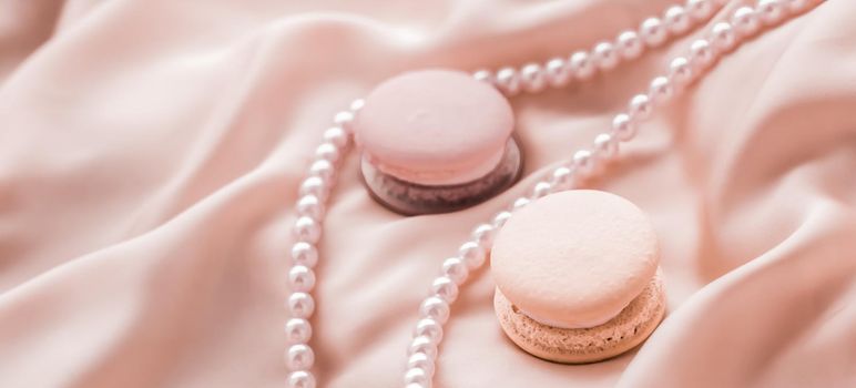 Girly, bakery and branding concept - Sweet macaroons and pearls jewellery on silk background, parisian chic jewelry, French dessert food and cake macaron for luxury confectionery brand, holiday gift