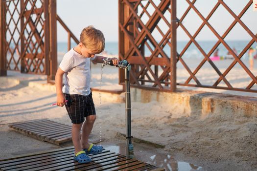 Child wash legs after beach sand Caucasian boy standing beach. Childhood summertime. Family vacation with one child.