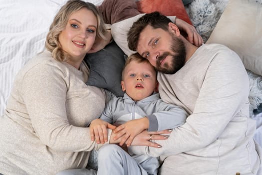 Happy family concept Mother father and little son have fun at home Caucasian family indoors Pregnant mom beard dad and funny little boy lie on the couch