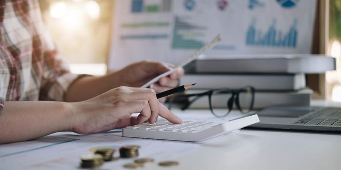 Financial data analyzing hand writing and counting on calculator in office on wood desk.