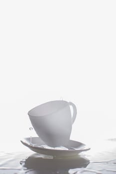 White cup and saucer with splashes of water.Vertical photograph of glass and water on a white background.