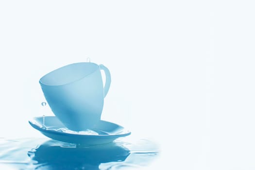 Blue cup and saucer with splashes of water.Glasses and water on a blue background