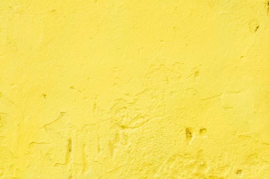 A close-up of a fragment of an old wall with rough, bright yellow plaster.