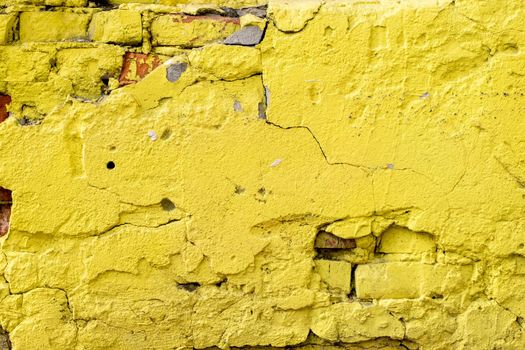 Close-up of a fragment of an old wall with rough plaster and bright yellow brickwork.