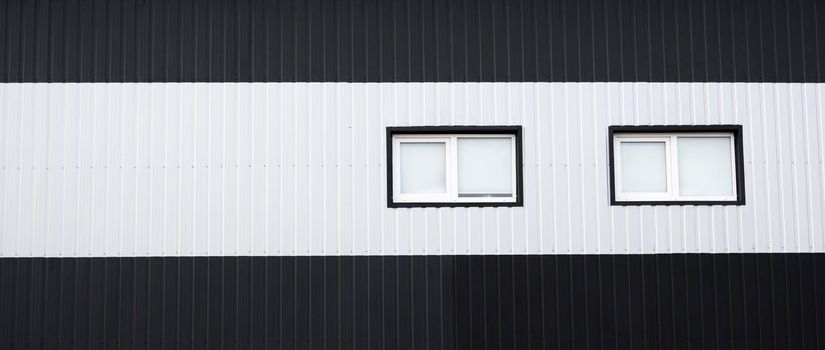 Black and white corrugated iron sheet used as a facade of a warehouse or factory with a windows. Texture of a seamless corrugated zinc sheet metal aluminum facade. Architecture. Metal texture