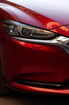 Fragment of a modern red car, headlight and bumper. Close up