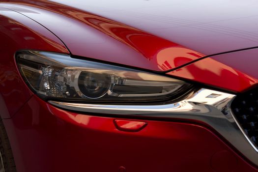 Fragment of a modern red car, headlight and bumper. Close up