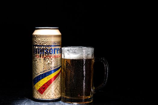 Can of Timisoareana beer and beer glass on dark background. Illustrative editorial photo shot in Bucharest, Romania, 2021