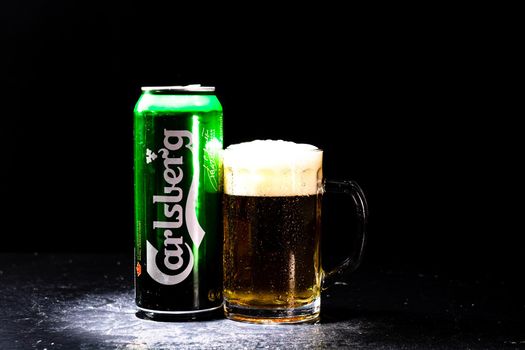 Can of Carlsberg beer and beer glass on dark background. Illustrative editorial photo shot in Bucharest, Romania, 2021