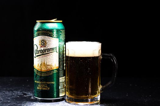 Can of Staropramen beer and beer glass on dark background. Illustrative editorial photo shot in Bucharest, Romania, 2021