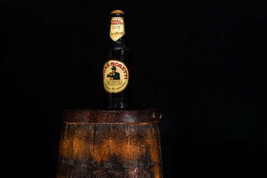 Bottle of Birra Moretti beer on wooden barrel with dark background. Illustrative editorial photo Bucharest, Romania, 2021