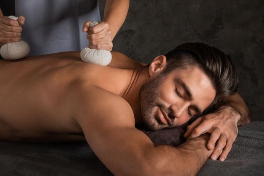 Young handsome man having back massage with pouche