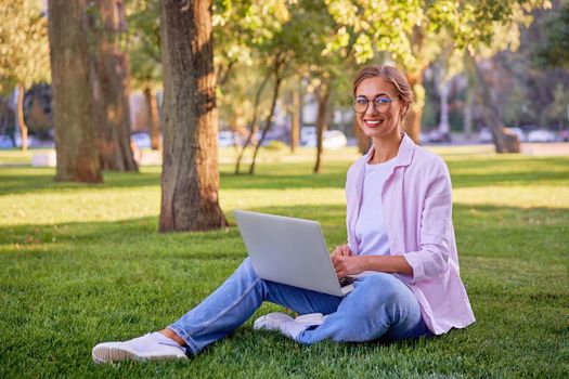 Businesswoman sitting grass summer park using laptop Business person working remote. Outdoor Successful european caucasian woman freelancer make video call teacher study work online lessons