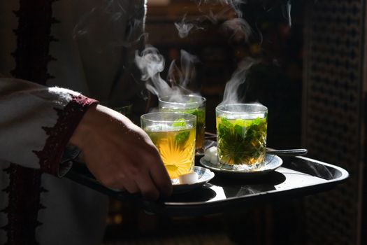 Traditional Moroccan mint tea in glasses steaming and backlit by sun being served on tray in a riad in Marrakech . High quality photo