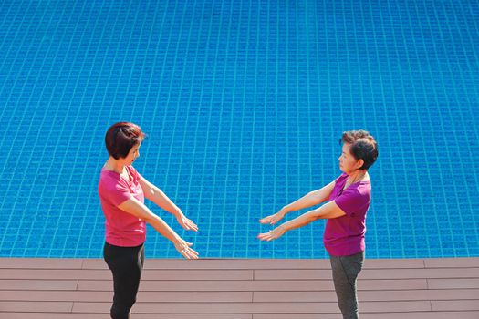 elderly woman doing exercise with daughter at pool patio