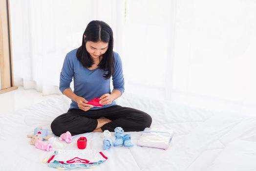 Asian mother preparing baby clothes resting and relaxing on the bed she makes purchase new baby clothes for after baby getting ready for newborn birth