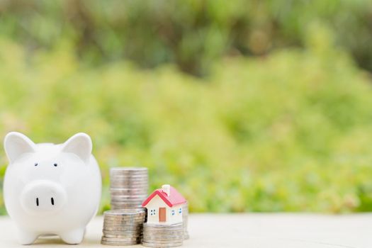 Piggy bank with house on stack of coins on blurred green natural background. Saving money and investment concept.