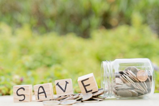 Save word on wooden block and jar full of coins on blurred green natural background. Saving money and investment concept.
